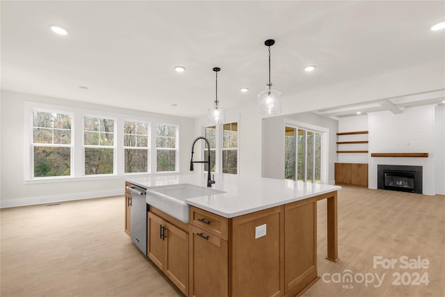 kitchen featuring a wealth of natural light, a fireplace, an island with sink, and pendant lighting