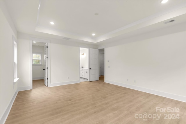 unfurnished bedroom with a tray ceiling, connected bathroom, a walk in closet, and light hardwood / wood-style flooring