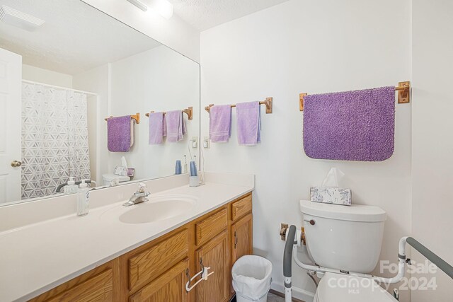 bathroom with vanity, toilet, curtained shower, and a textured ceiling