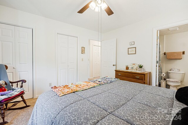 carpeted bedroom with two closets, ensuite bathroom, and ceiling fan