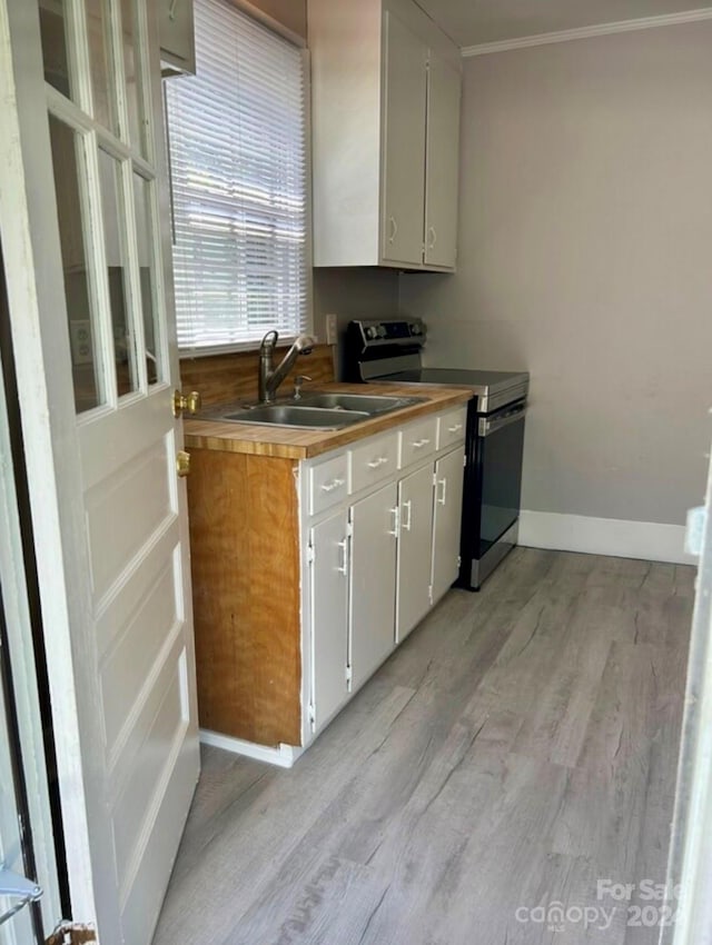 kitchen with white cabinets, crown molding, light hardwood / wood-style flooring, sink, and stainless steel range with electric cooktop