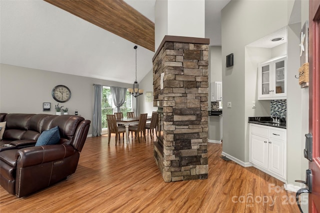 living room with sink, an inviting chandelier, high vaulted ceiling, beamed ceiling, and light wood-type flooring