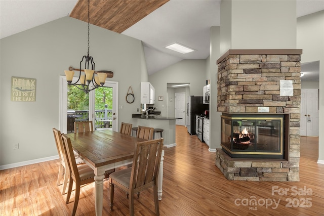 dining room with a fireplace, light hardwood / wood-style flooring, high vaulted ceiling, and a chandelier