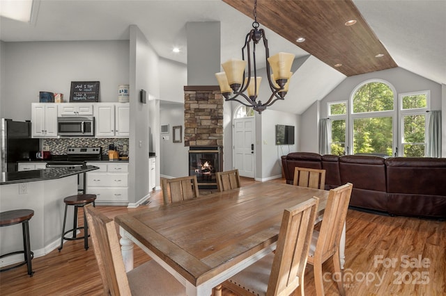 dining space featuring lofted ceiling, a chandelier, a fireplace, and light hardwood / wood-style floors