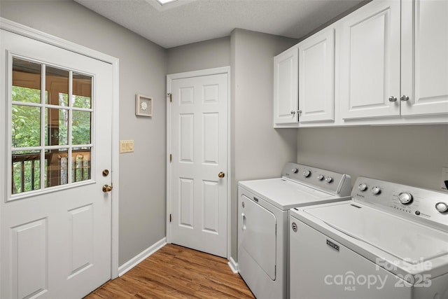 laundry area featuring separate washer and dryer, cabinets, a textured ceiling, and light wood-type flooring