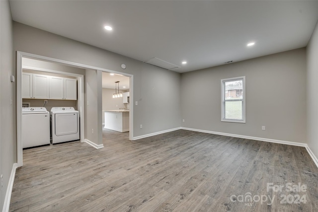 unfurnished living room with an inviting chandelier, light wood-type flooring, and washing machine and dryer