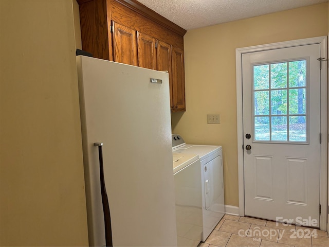 washroom featuring a textured ceiling, washing machine and clothes dryer, light tile patterned floors, and cabinets