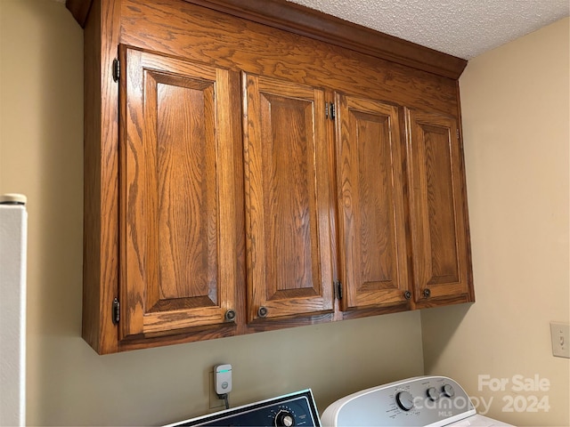 laundry area with washer / dryer, a textured ceiling, and cabinets