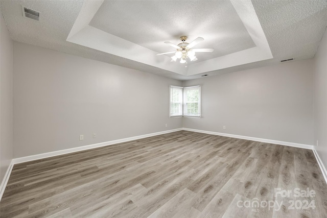 spare room with light hardwood / wood-style floors, ceiling fan, a raised ceiling, and a textured ceiling