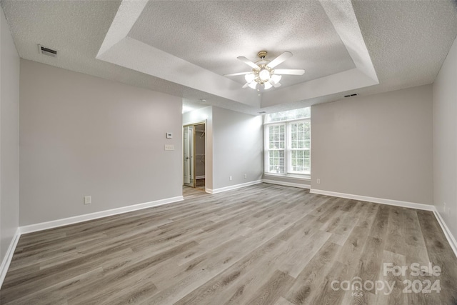 spare room featuring ceiling fan, a textured ceiling, light hardwood / wood-style flooring, and a raised ceiling