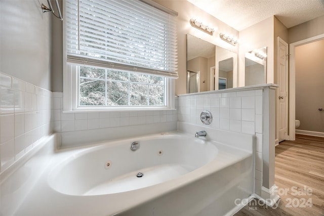 bathroom with wood-type flooring, a textured ceiling, a bathtub, and toilet