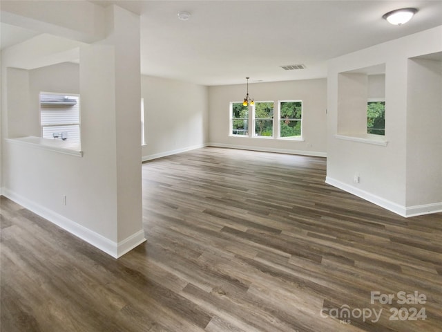 unfurnished living room featuring an inviting chandelier and dark wood-type flooring