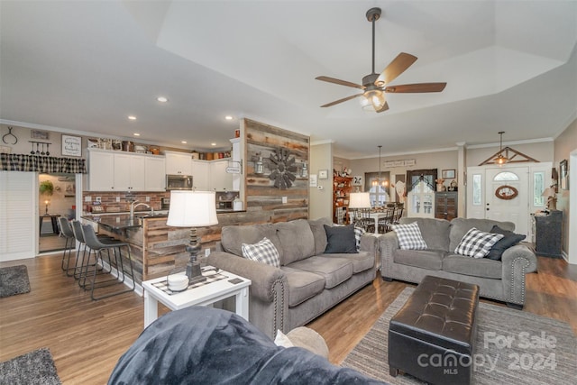 living room with wood-type flooring, ornamental molding, sink, and ceiling fan