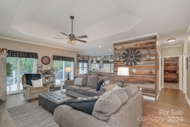 living room featuring ceiling fan, wood walls, ornamental molding, light hardwood / wood-style flooring, and a tray ceiling