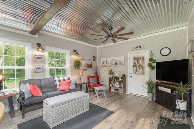 living room featuring wood-type flooring, wood walls, beam ceiling, and ceiling fan