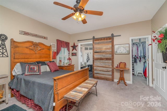 carpeted bedroom with a closet, ceiling fan, a walk in closet, and a barn door