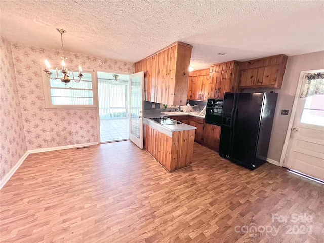 kitchen with pendant lighting, light wood-type flooring, black appliances, a textured ceiling, and a chandelier