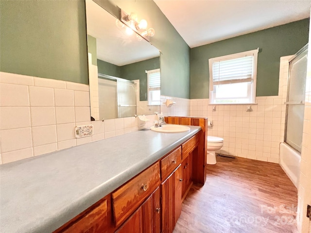 full bathroom featuring tile walls, wood-type flooring, combined bath / shower with glass door, vanity, and toilet