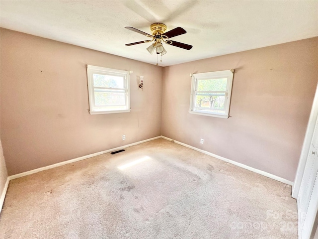 carpeted empty room with ceiling fan and plenty of natural light