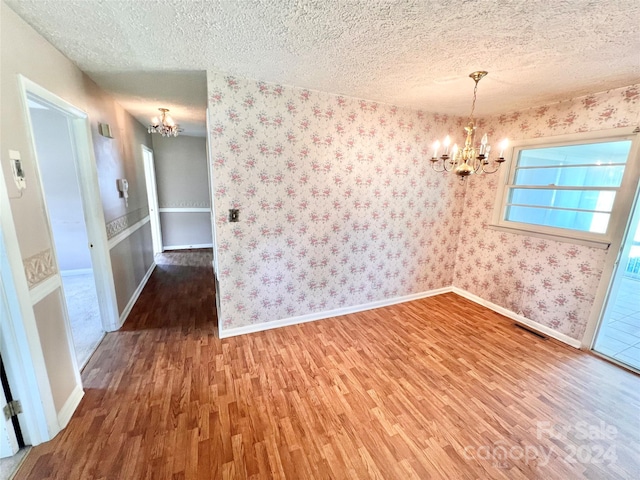 unfurnished room with a textured ceiling, a chandelier, and hardwood / wood-style floors