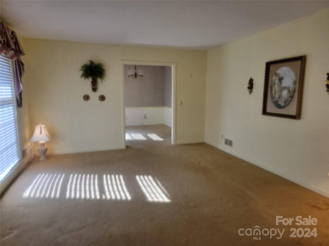 carpeted spare room featuring an inviting chandelier