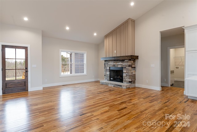 unfurnished living room with a stone fireplace, lofted ceiling, and light wood-type flooring