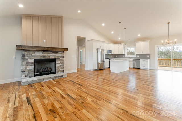 unfurnished living room with light hardwood / wood-style floors, a stone fireplace, high vaulted ceiling, and a chandelier