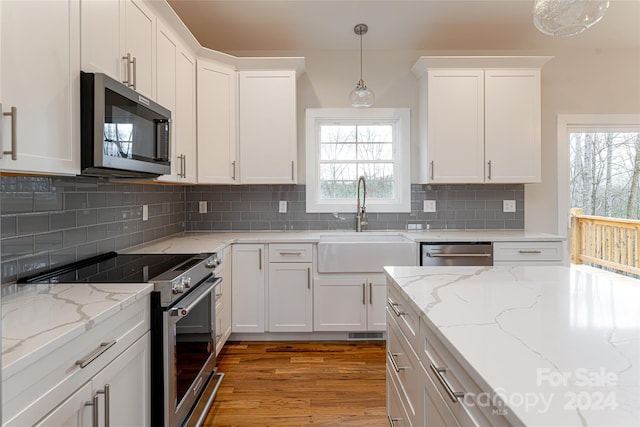 kitchen with hanging light fixtures, hardwood / wood-style flooring, appliances with stainless steel finishes, tasteful backsplash, and white cabinetry