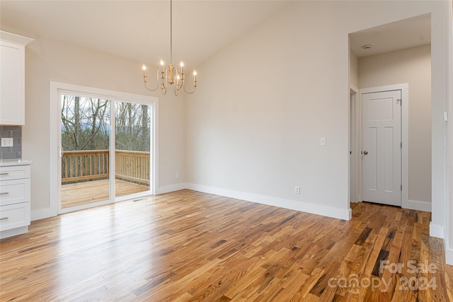 unfurnished dining area featuring a chandelier, vaulted ceiling, and light hardwood / wood-style flooring