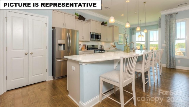 kitchen featuring crown molding, decorative light fixtures, appliances with stainless steel finishes, a kitchen breakfast bar, and an island with sink