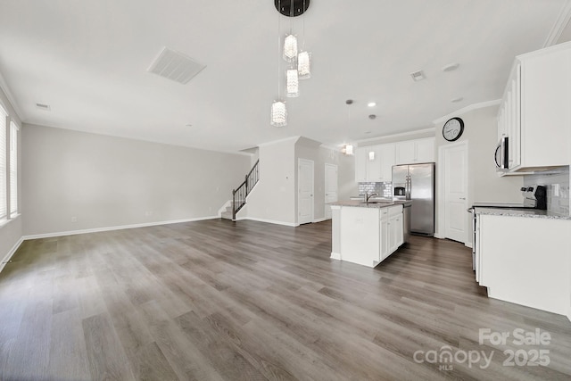 kitchen featuring white cabinetry, a center island with sink, appliances with stainless steel finishes, decorative backsplash, and pendant lighting