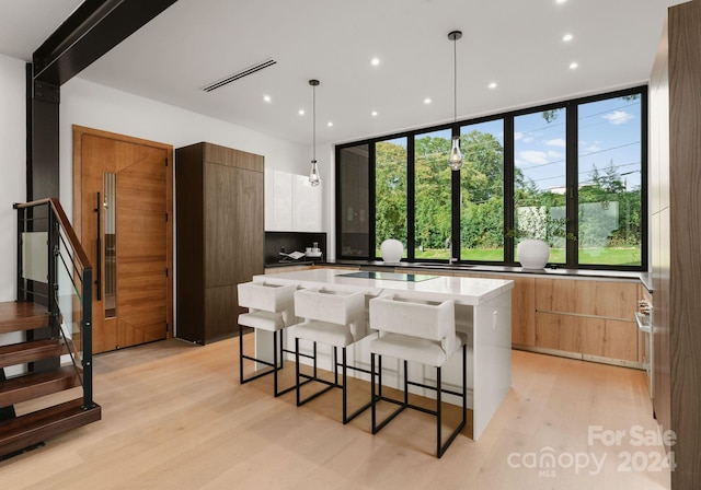 kitchen with light stone counters, hanging light fixtures, light hardwood / wood-style floors, white cabinets, and a center island