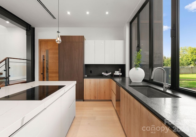 kitchen featuring white cabinets, hanging light fixtures, sink, backsplash, and light wood-type flooring