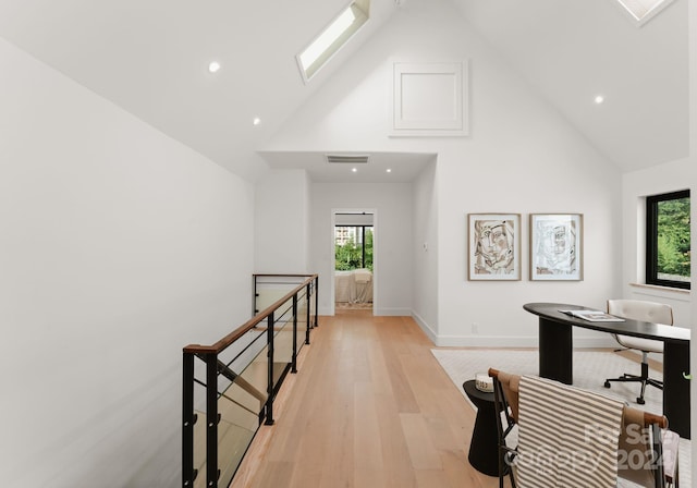 hall with high vaulted ceiling, plenty of natural light, and light hardwood / wood-style flooring