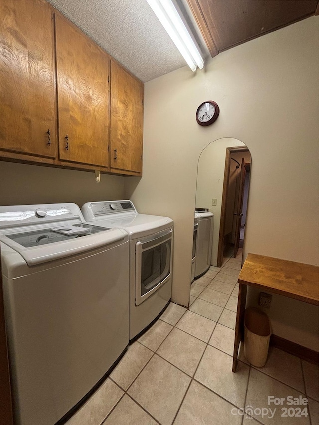 laundry area with a textured ceiling, washer and clothes dryer, light tile patterned floors, and cabinets