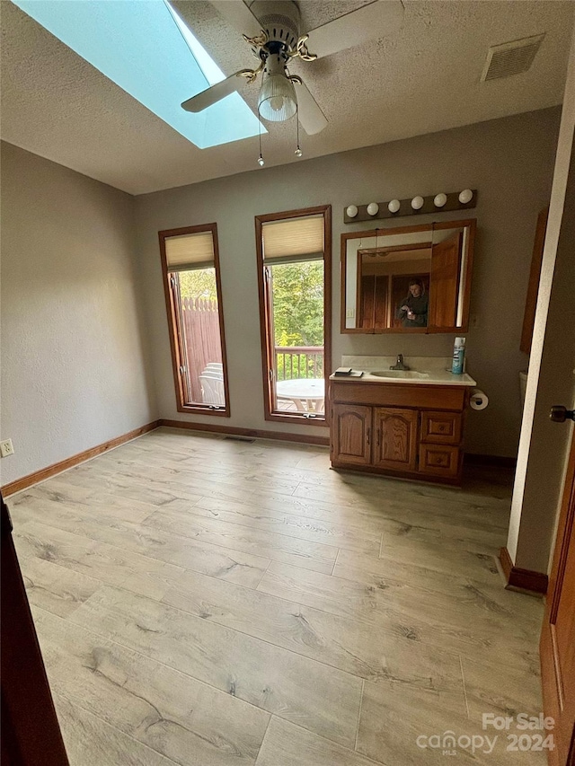 interior space featuring a textured ceiling, ceiling fan, a skylight, light hardwood / wood-style flooring, and sink