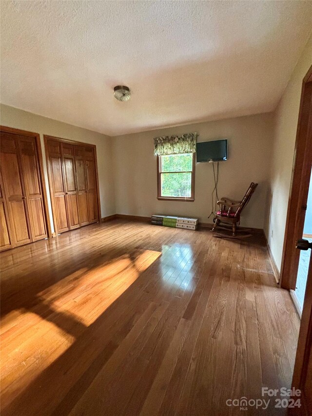 interior space with a textured ceiling, hardwood / wood-style floors, and multiple closets