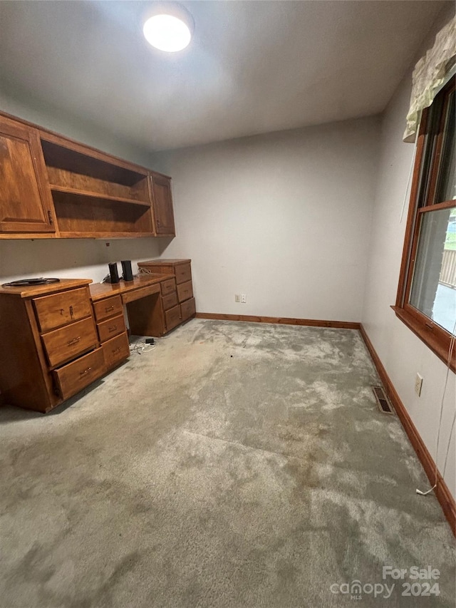 unfurnished office featuring built in desk and light colored carpet