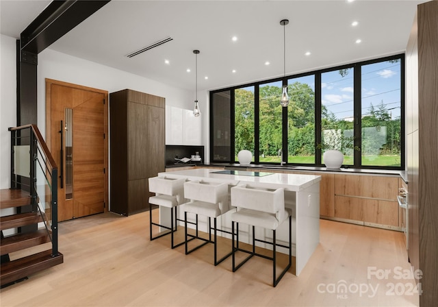 kitchen featuring pendant lighting, white cabinets, a center island, light stone countertops, and light hardwood / wood-style floors