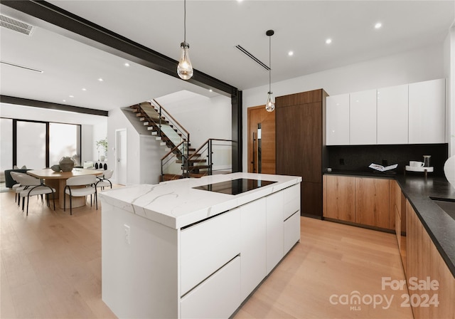 kitchen featuring light hardwood / wood-style floors, white cabinetry, a kitchen island, decorative light fixtures, and black electric cooktop