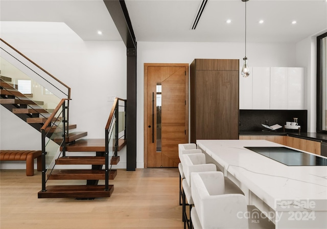 kitchen with white cabinets, dark stone counters, pendant lighting, light wood-type flooring, and black electric stovetop