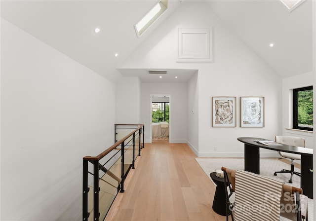 office with light hardwood / wood-style floors, high vaulted ceiling, a skylight, and plenty of natural light