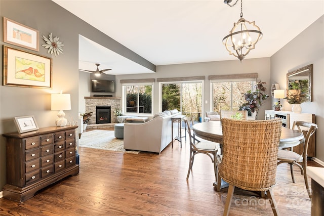 dining space featuring a stone fireplace, ceiling fan with notable chandelier, and hardwood / wood-style flooring