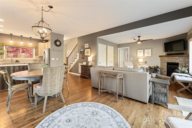 dining space with ceiling fan with notable chandelier, hardwood / wood-style flooring, a stone fireplace, and sink