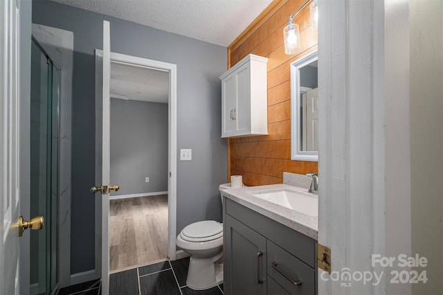 bathroom with a shower with shower door, vanity, a textured ceiling, hardwood / wood-style flooring, and toilet