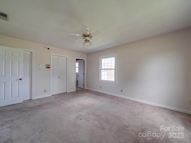 unfurnished bedroom featuring two closets, light colored carpet, a textured ceiling, and ceiling fan