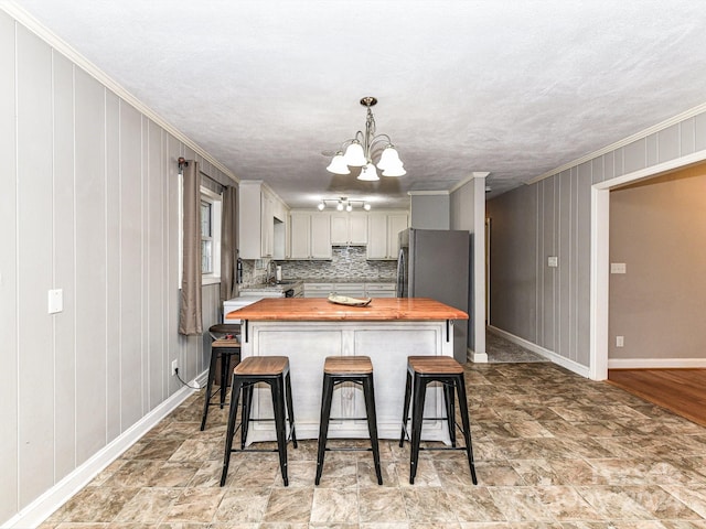 kitchen featuring pendant lighting, tasteful backsplash, an inviting chandelier, crown molding, and wood counters