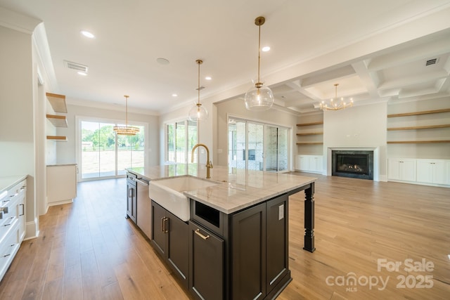 kitchen with pendant lighting, sink, light stone countertops, an island with sink, and light wood-type flooring