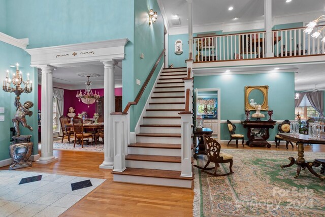 stairway featuring an inviting chandelier, hardwood / wood-style flooring, ornamental molding, and ornate columns