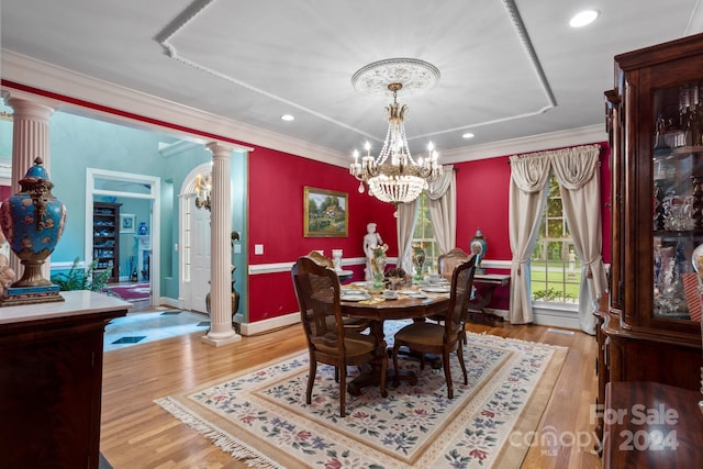 dining area with crown molding, decorative columns, an inviting chandelier, and light hardwood / wood-style flooring